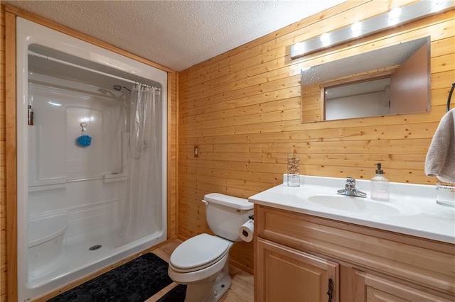 bathroom with a textured ceiling, toilet, wooden walls, vanity, and a stall shower