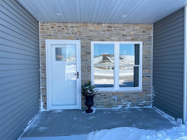 snow covered property entrance with stone siding