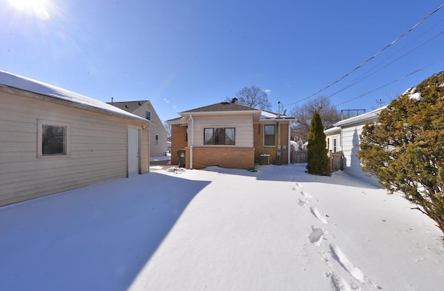 snow covered property with a garage, brick siding, and central AC unit