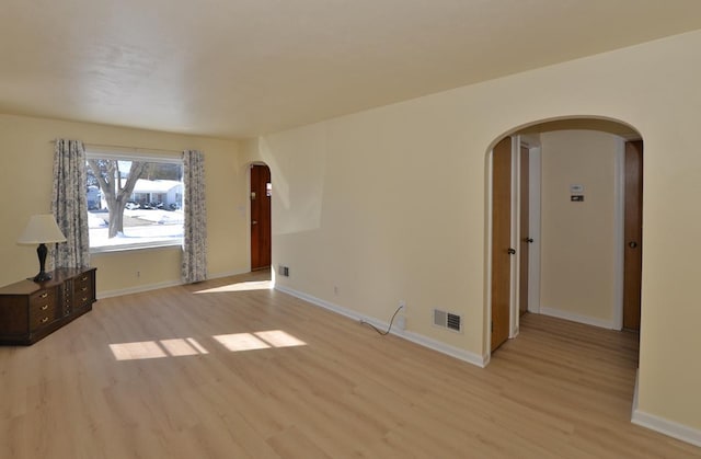 spare room with light wood-type flooring, arched walkways, visible vents, and baseboards