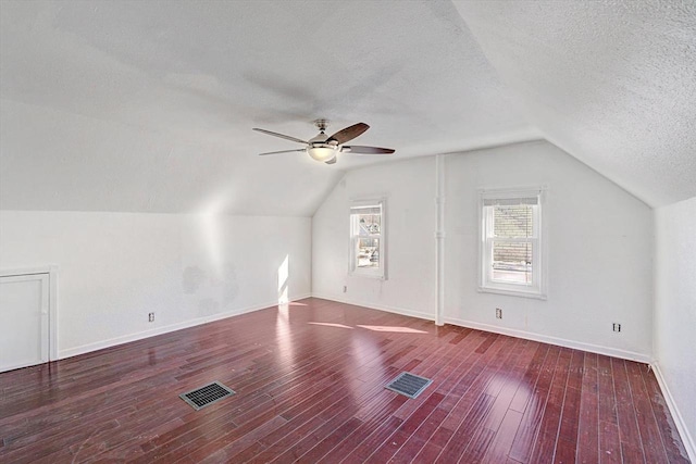 bonus room with lofted ceiling, visible vents, dark wood-type flooring, and a textured ceiling