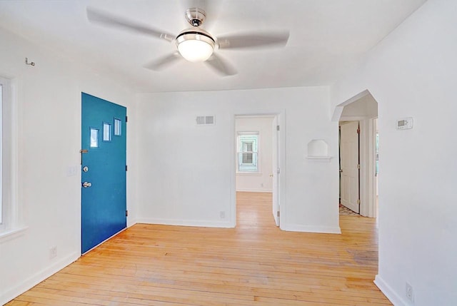 empty room featuring arched walkways, light wood finished floors, visible vents, ceiling fan, and baseboards