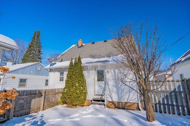 snow covered back of property with entry steps, a chimney, and fence