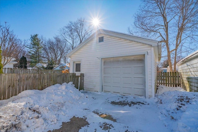 snow covered garage with a detached garage and fence