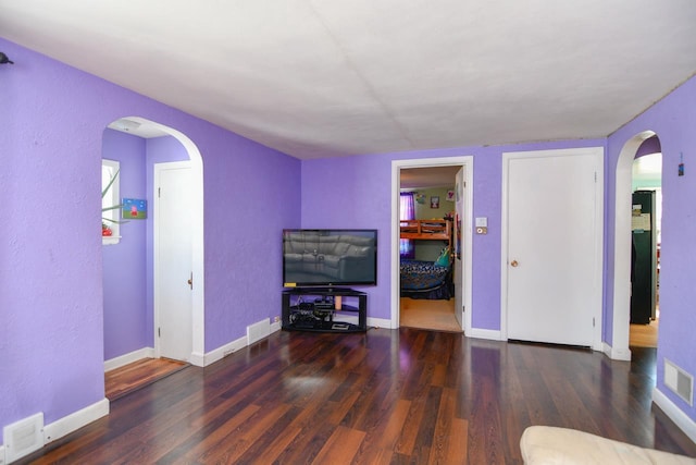 living area featuring arched walkways, dark wood finished floors, visible vents, and baseboards