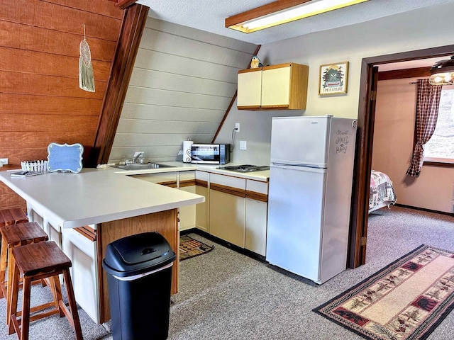 kitchen with a kitchen breakfast bar, freestanding refrigerator, a peninsula, light countertops, and wood walls