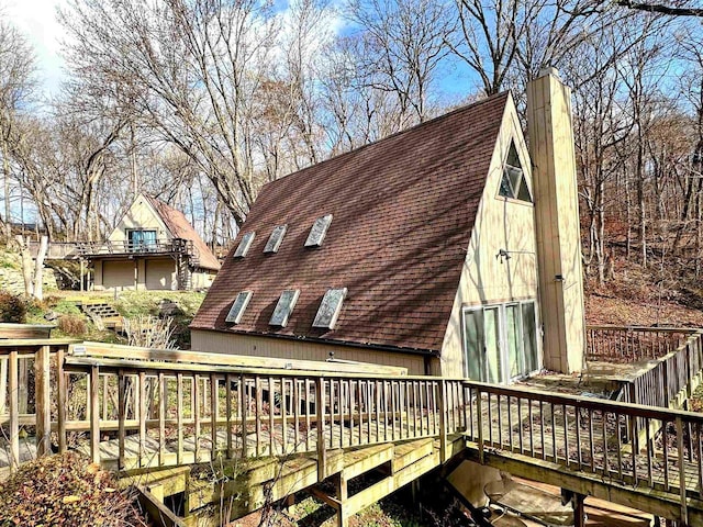 exterior space with a shingled roof, a chimney, and a deck