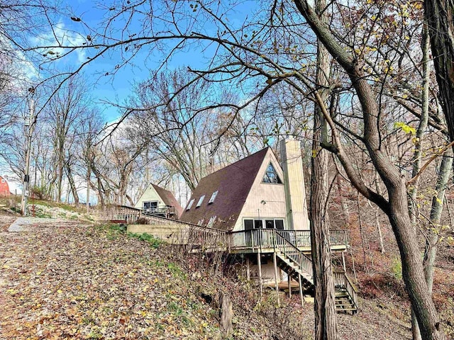 view of home's exterior featuring a deck, a chimney, a shingled roof, and stairway