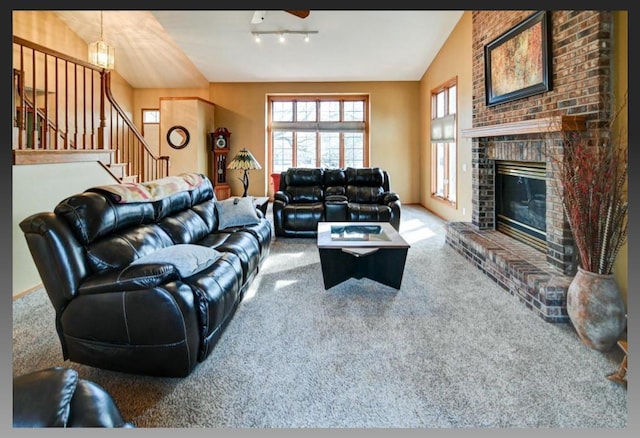 carpeted living area with stairway, a fireplace, ceiling fan, and vaulted ceiling