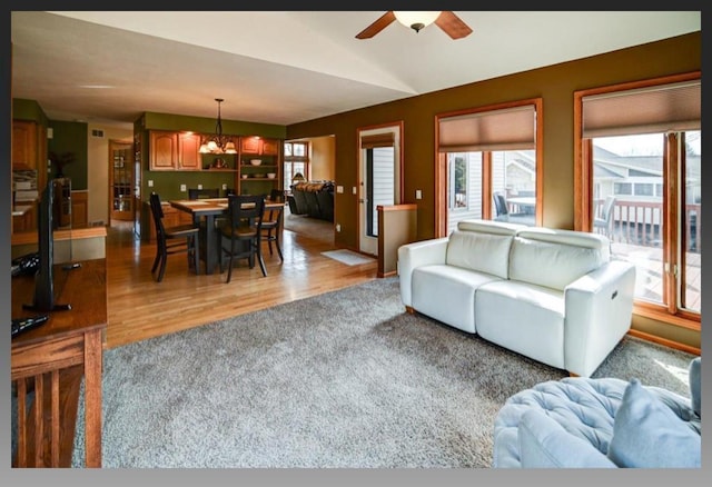 living area with ceiling fan with notable chandelier, light wood-style floors, and lofted ceiling