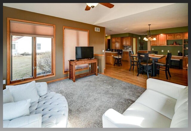 living room with visible vents, baseboards, light wood-style floors, and ceiling fan with notable chandelier