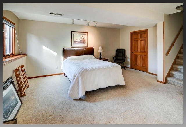 carpeted bedroom featuring a glass covered fireplace, track lighting, baseboards, and visible vents