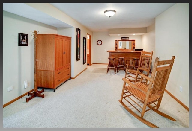 sitting room featuring light carpet, a bar, and baseboards