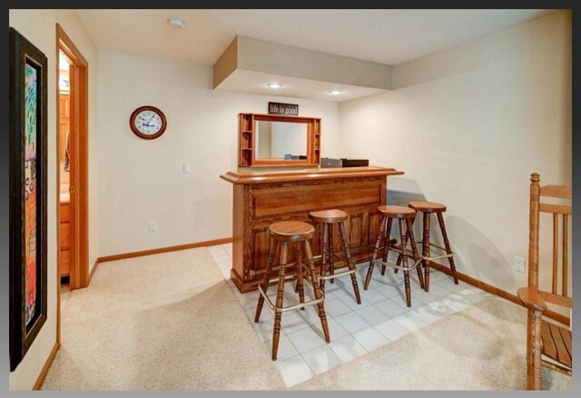 bar with light colored carpet, baseboards, and a bar