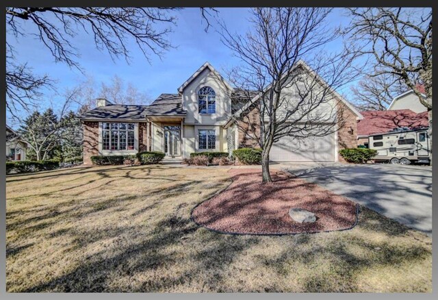 view of front of home with brick siding, a front yard, an attached garage, and driveway