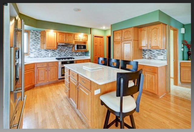 kitchen with under cabinet range hood, a kitchen breakfast bar, a center island, light wood-style floors, and appliances with stainless steel finishes