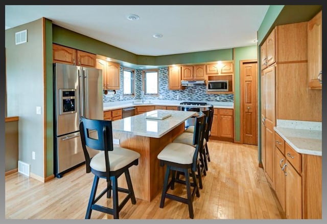 kitchen featuring visible vents, a kitchen island, light countertops, decorative backsplash, and appliances with stainless steel finishes