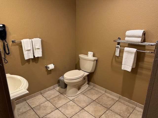half bathroom with toilet, baseboards, and tile patterned floors