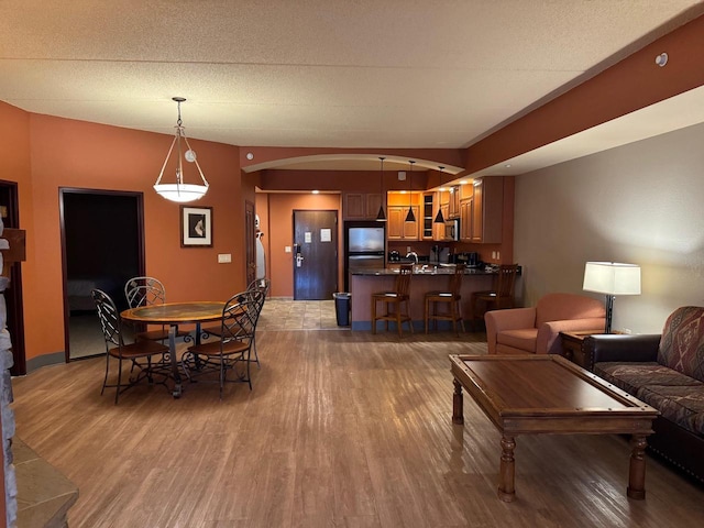 dining area with a textured ceiling, arched walkways, and wood finished floors