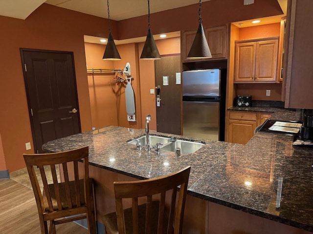 kitchen featuring a breakfast bar, hanging light fixtures, freestanding refrigerator, a sink, and a peninsula