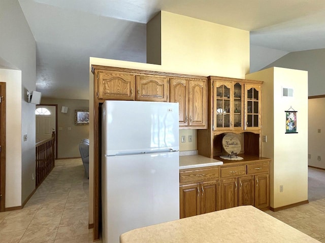 kitchen featuring brown cabinets, light countertops, visible vents, glass insert cabinets, and freestanding refrigerator