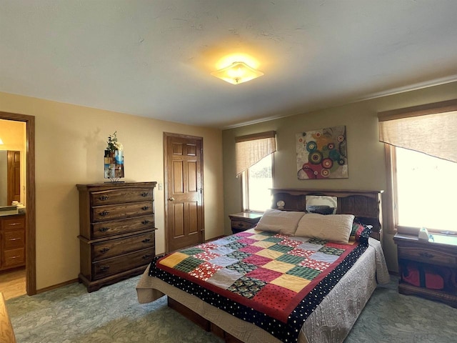 bedroom with baseboards, connected bathroom, and light colored carpet