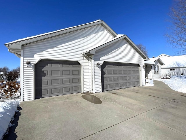 snow covered garage featuring concrete driveway