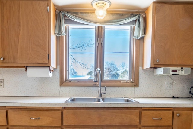 kitchen featuring brown cabinets, decorative backsplash, light countertops, and a sink