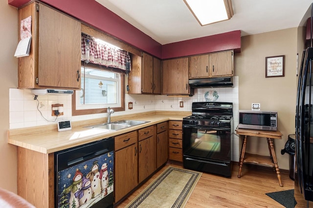 kitchen with under cabinet range hood, a sink, light countertops, brown cabinets, and black appliances