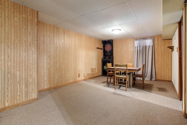 dining area featuring baseboards, light carpet, wood walls, and a drop ceiling