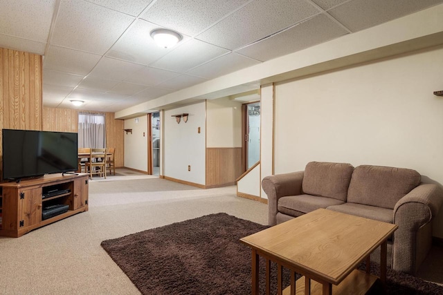 living area featuring baseboards, light carpet, wood walls, and a drop ceiling