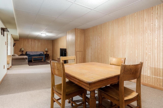 dining space with wooden walls, a drop ceiling, and light colored carpet