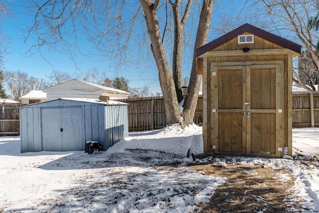 snow covered structure with an outbuilding, fence, and a shed