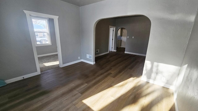 unfurnished room with baseboards, visible vents, arched walkways, and dark wood finished floors