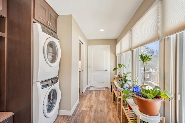 washroom featuring light wood-type flooring, stacked washer and dryer, and baseboards