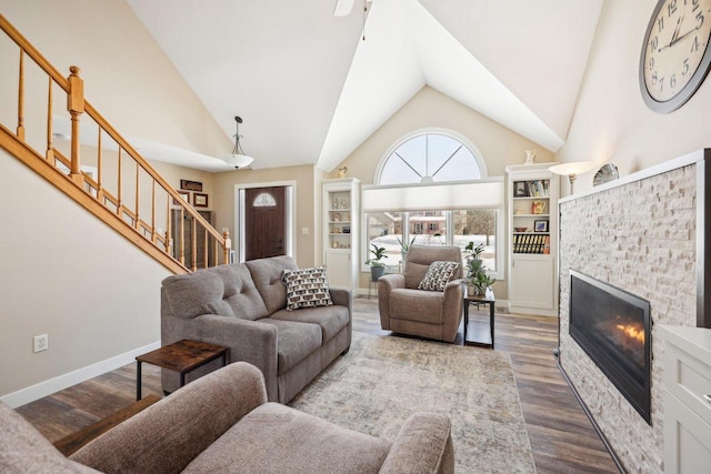 living area with stairs, high vaulted ceiling, a fireplace, and wood finished floors