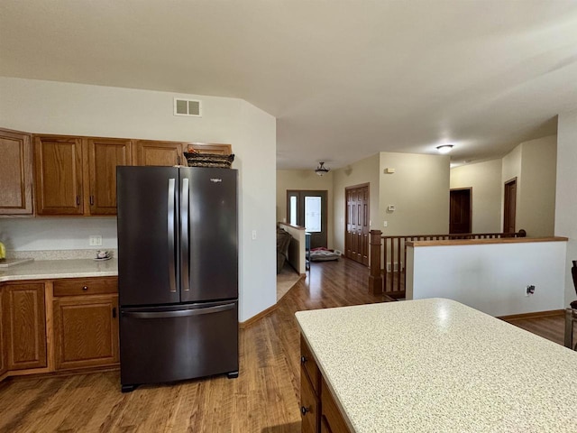 kitchen featuring light countertops, visible vents, brown cabinetry, freestanding refrigerator, and wood finished floors