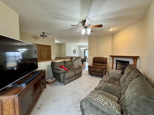 living room featuring ceiling fan with notable chandelier, carpet floors, and a fireplace