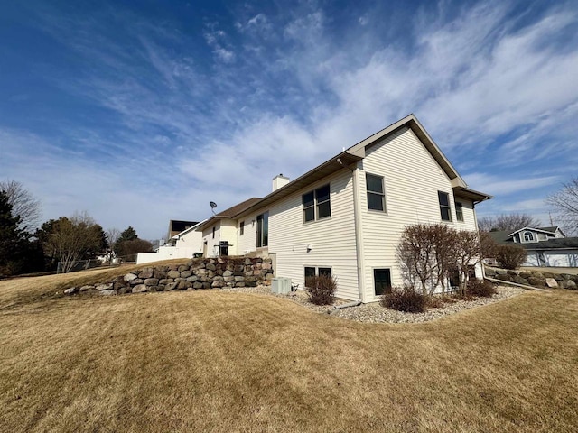 view of side of property with a chimney, central AC, and a lawn