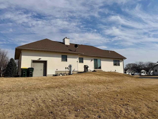 back of house with an attached garage, a chimney, and a yard