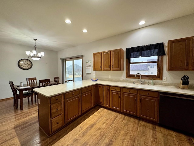 kitchen with dishwashing machine, a peninsula, a sink, light countertops, and light wood-type flooring