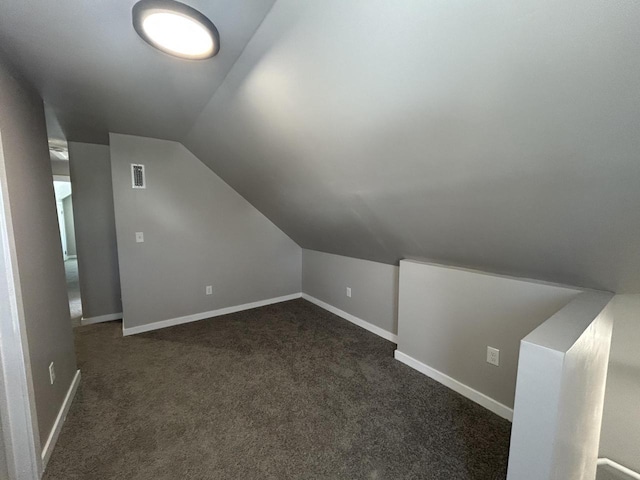 additional living space with dark colored carpet, visible vents, vaulted ceiling, and baseboards