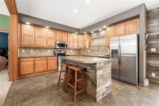 kitchen with appliances with stainless steel finishes, a center island, decorative backsplash, and a kitchen bar