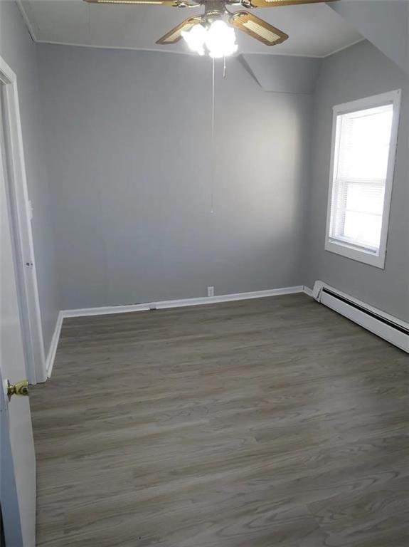 spare room featuring a baseboard radiator, wood finished floors, a ceiling fan, and baseboards