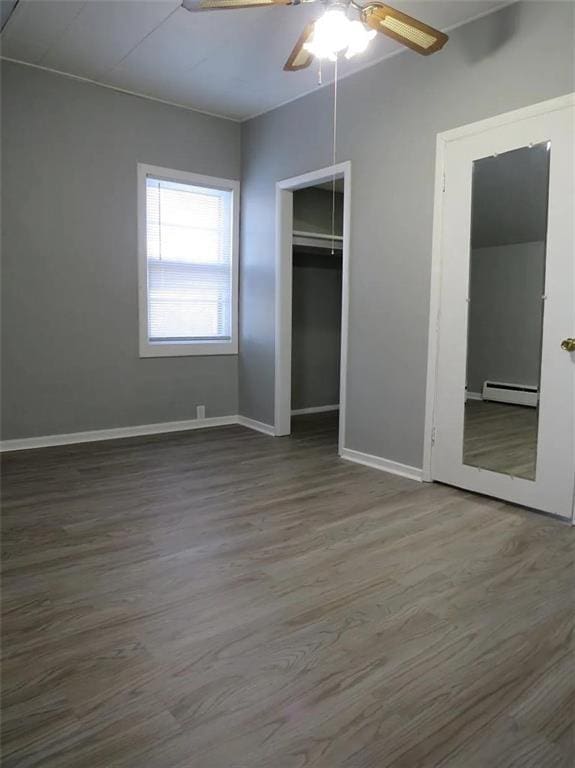 unfurnished bedroom with a baseboard radiator, a closet, a ceiling fan, wood finished floors, and baseboards