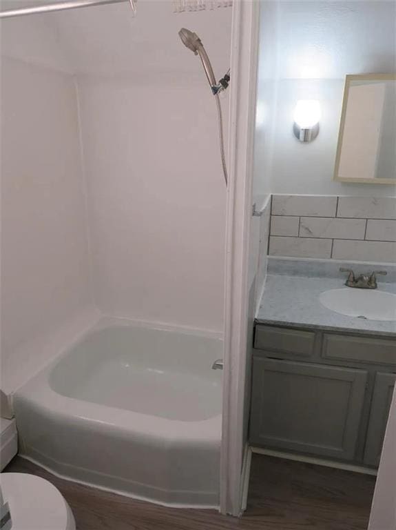 bathroom featuring shower / tub combination, toilet, wood finished floors, vanity, and decorative backsplash