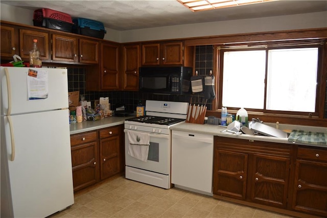 kitchen featuring light floors, tasteful backsplash, light countertops, a sink, and white appliances