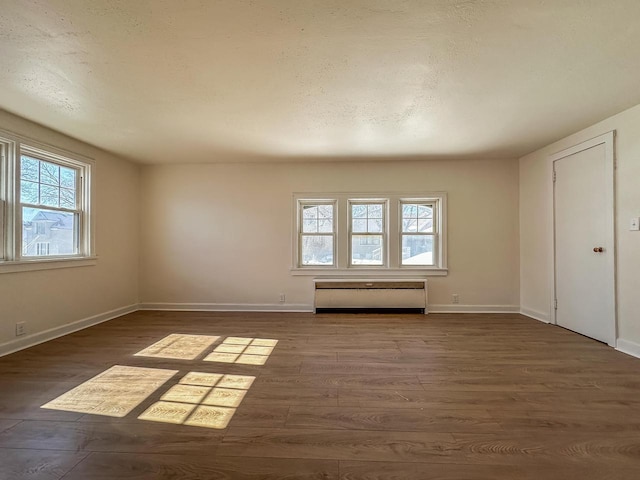 unfurnished room with a textured ceiling, a baseboard heating unit, dark wood-style flooring, and baseboards