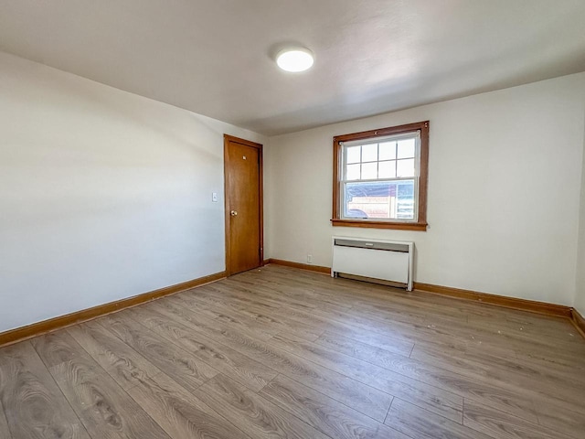 spare room with radiator heating unit, light wood-type flooring, and baseboards