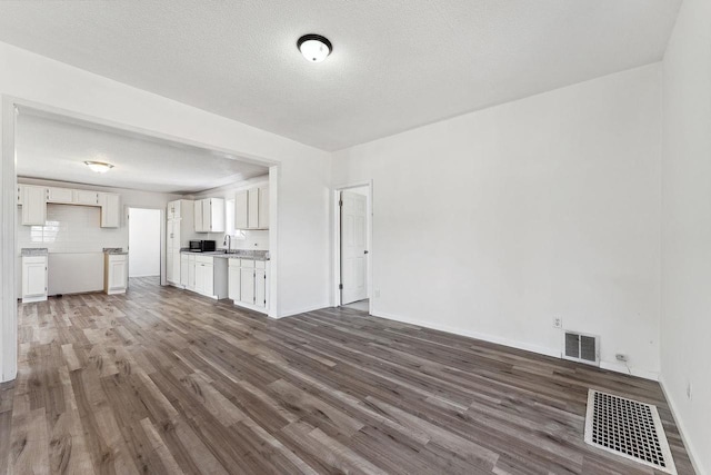 unfurnished living room with visible vents, a textured ceiling, and wood finished floors